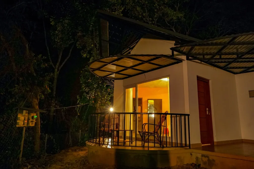 Cozy forest cottage with warm interior lighting and private balcony seating at night, offering a peaceful stay at the best resort in Wayanad.