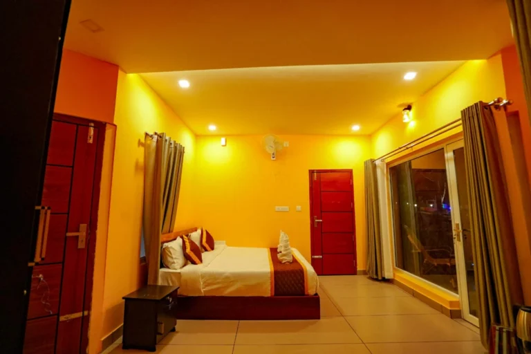 Spacious air-conditioned bedroom with balcony view, warm lighting, and modern interiors at the best resort in Wayanad.