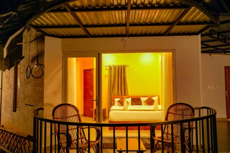 Luxury cottage bedroom with warm ambient lighting and private balcony seating at night, showcasing a relaxing stay at the best resort in Wayanad.