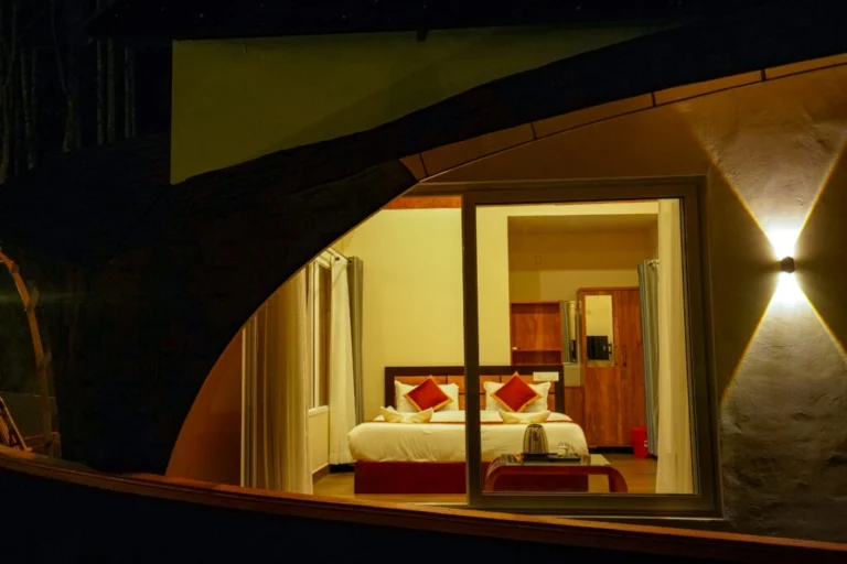 Cozy luxury bedroom viewed through modern cottage window with warm lighting at the best resort in Wayanad.