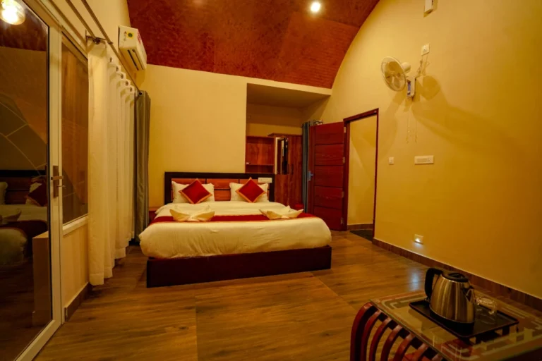 Spacious luxury bedroom with wooden flooring, warm ambient lighting, and modern amenities at the best resort in Wayanad.